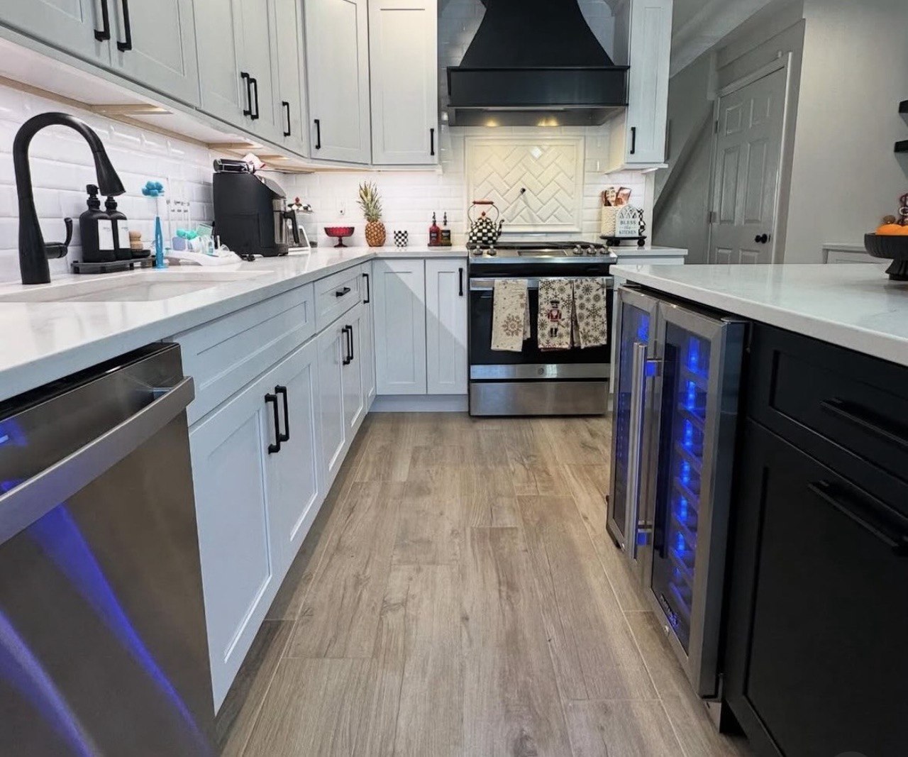 Kitchen with pale cabinets, black accents and blue-lit beverage cooler.